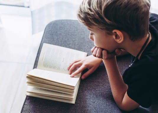 Kind liest Buch auf Sofa